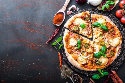 tasty pizza on a black background with spices and vegetables