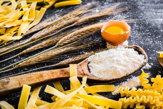 uncooked pasta, flour and other products on a black textured table