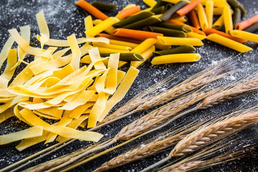 uncooked pasta, flour and other products on a black textured table