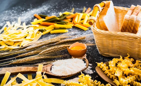 uncooked pasta, bread and other products on a black textured table