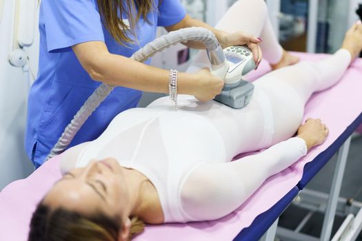 Middle-aged woman in special white suit having a anti cellulite belly massage with spa apparatus