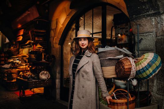 a girl in a coat and hat stands near baskets in the old town of Annecy,An elegant young lady in a coat and hat enjoys a view of the old town in France.
