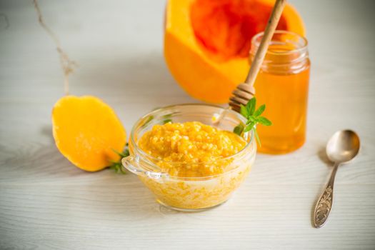 sweet boiled pumpkin porridge in a bowl with honey on a light wooden table