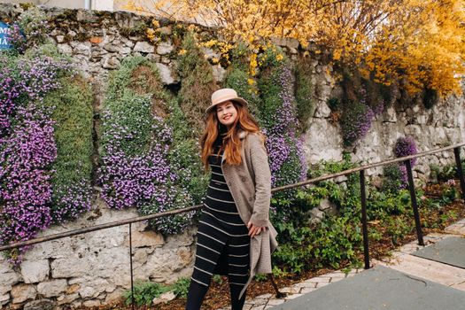 a beautiful romantic girl in a coat and hat walks in Annecy. France. Girl in a hat in France on the background of flowering plants.