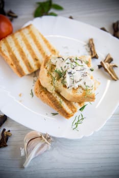 fried bread toast with cheese spread with boiled dried mushrooms, in a plate on a wooden table.