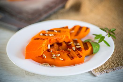 sweet baked grilled pumpkin with seeds in a plate on a wooden table