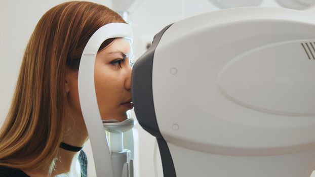 Ophthalmology clinic concept - young attractive female doing checking vision by modern electronic technology, close up