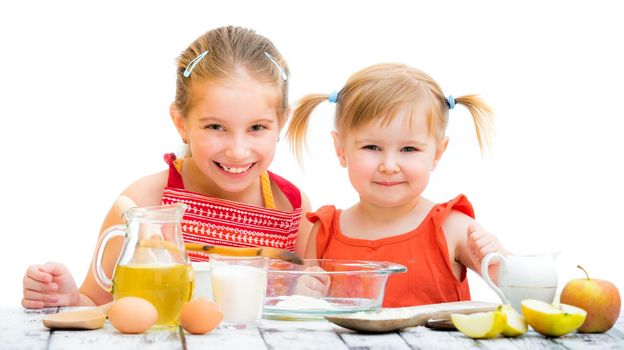 two cute little sisters cooking and looking into the camera on a white background