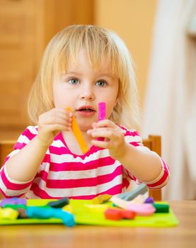 Smiling girl playing with plasticine at home