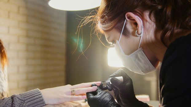 Manual labour - professional manicurist - nail master in medical mask doing professional manicure, telephoto, close up