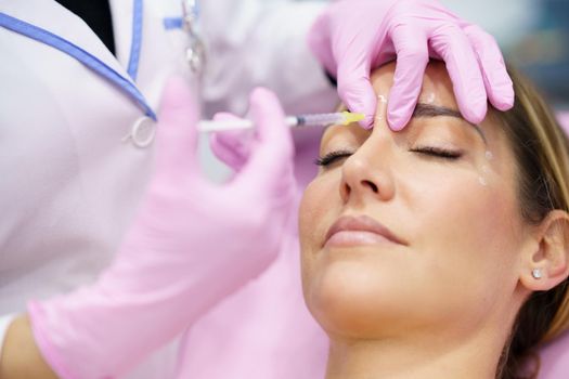 Aesthetic doctor injecting botulinum toxin into the forehead of her middle-aged patient. Facial treatment done in a cosmetic surgery clinic.