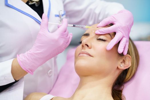 Aesthetic doctor injecting botox into the forehead of her middle-aged patient. Facial treatment done in a cosmetic surgery clinic.
