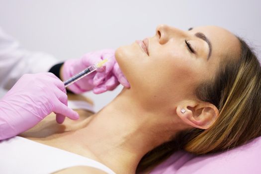 Doctor injecting hyaluronic acid into the chin of a middle-aged woman as a facial rejuvenation treatment.