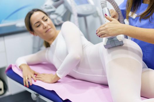 Middle-aged woman in special white suit having a anti cellulite massage with spa apparatus