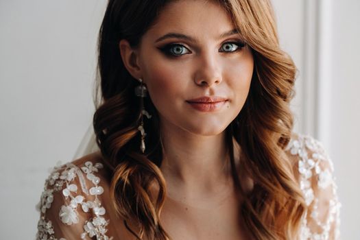 Close-up portrait of a luxurious bride in a wedding dress in the morning in her interior.