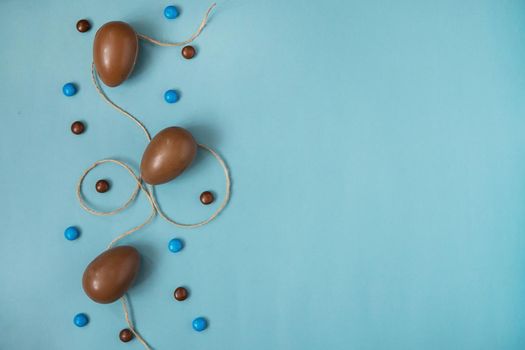 Flat lay composition with chocolate Easter eggs and chocolate sweets on blue background. View from above, empty space for text.