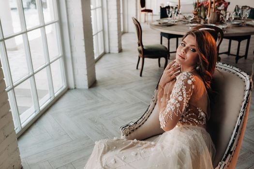 A luxurious bride in a wedding dress in the morning in her interior.