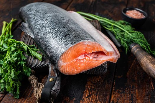 Big piece of Raw cut salmon fish on a wooden cutting board with chef knife. Dark Wooden background. Top view.