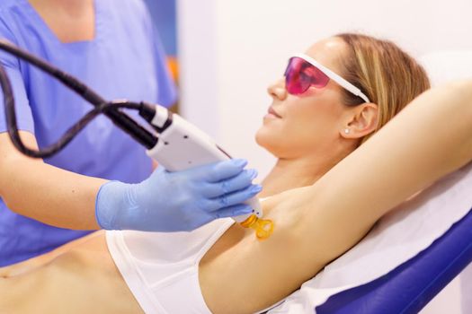 Woman receiving underarm laser hair removal at a beauty center. Laser depilation treatment in an aesthetic clinic.