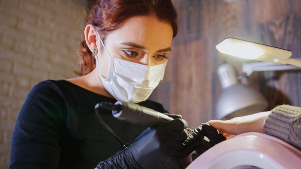 Woman manicurist in medical mask doing manicure in beauty salon, horizontal
