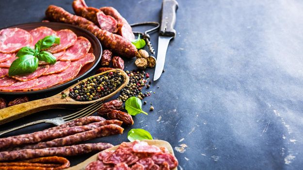 various sausages with spices on black table