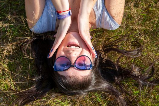 happy beautiful young woman in sunglasses smiles and lies on a meadow in the grass in the sunshine enjoy summer day