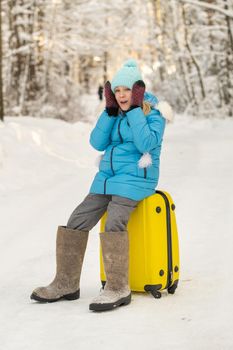 A girl in winter in felt boots sits on a suitcase on a frosty snowy day.