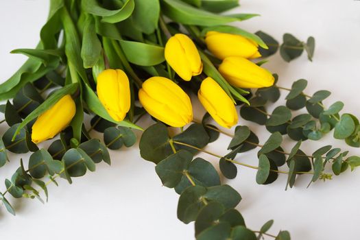 beautiful yellow tulips with eucalyptus branches on a white table