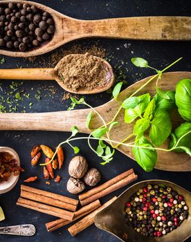 wooden spoons with spices and herbs on textured black background