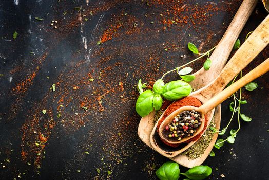 wooden spoons with spices and herbs on textured black background