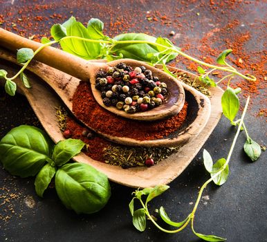 wooden spoons with spices and herbs on textured black background