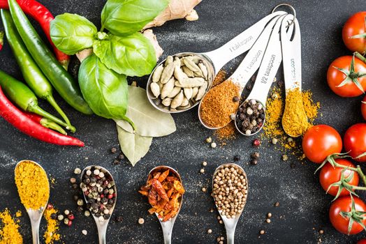 spoons with different spices and vegetables on a black table