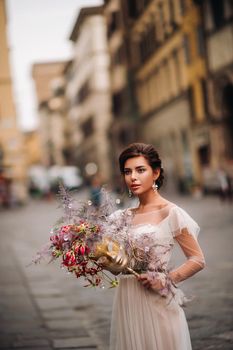 the girl-bride is with beautiful flower pattern as a mask in Florence, stylish bride in a wedding dress standing with a mask in the Old town of Florence. Model girl in Florence.