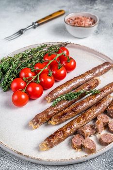 Grilled lamb meat sausage on a plate with herbs and tomato. White background. Top view.