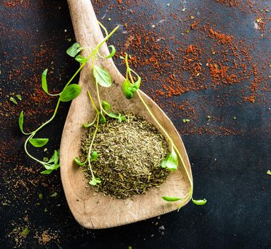 wooden spoons with spices and herbs on textured black background