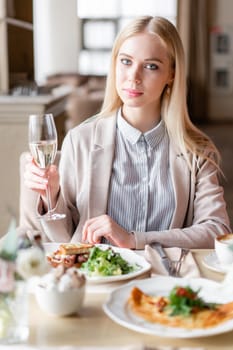 Portrait of a beautiful young elegant blonde woman in the cafe with a glass of champagne