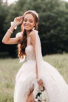 On the wedding day, an Elegant bride in a white long dress and gloves with a bouquet in her hands stands in a clearing enjoying nature. Belarus