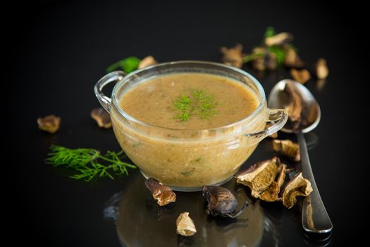 hot homemade vegetable vegetarian soup with dried mushrooms in a glass bowl on black background
