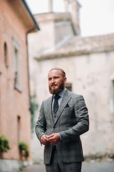 A man with a beard in a strict grey three-piece suit with a tie in the old town of Sirmione, a Stylish man in a grey suit in Italy.