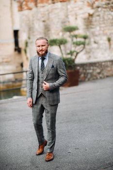 A man with a beard in a strict grey three-piece suit with a tie in the old town of Sirmione, a Stylish man in a grey suit in Italy.