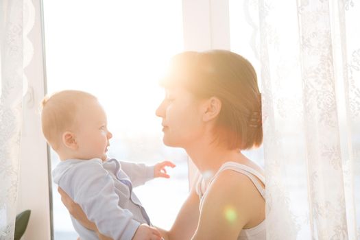 Happy mother holding adorable child baby with sunrise background