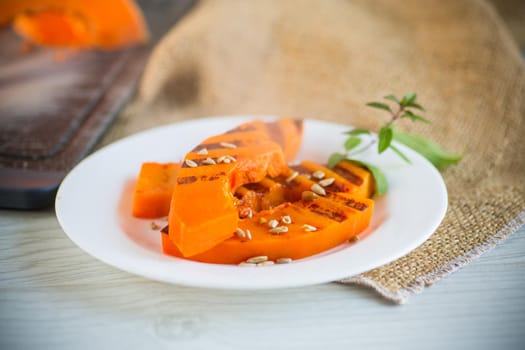 sweet baked grilled pumpkin with seeds in a plate on a wooden table
