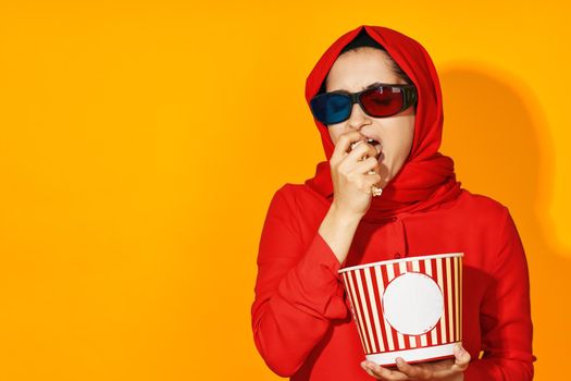 woman in red hijab 3d glasses technology watching movie popcorn yellow background. High quality photo