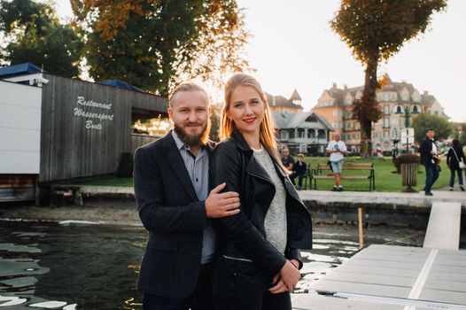 a family of two stands on a pier in Austria's old town at sunset .A man and a woman embrace on the embankment of a small town in Austria.Europe.Felden am Werten see.