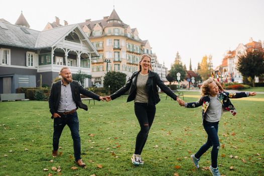 A happy family of three runs through the grass in Austria's old town.A family walks through a small town in Austria.Europe.Velden am werten Zee.