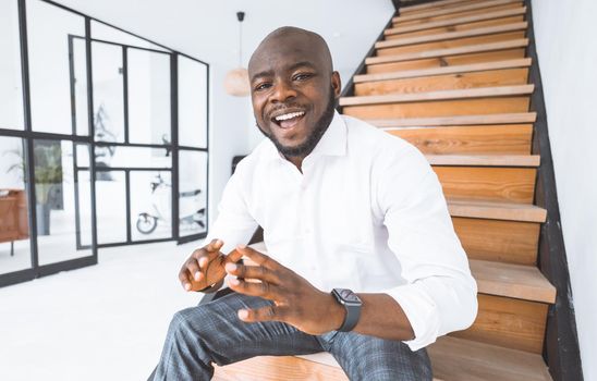 Successful Young Businessman. African American Guy Shares His Success Story. Young Man Sits On Stairs In His Luxurious Home. Concept Of Victory, Personal Growth. High Quality Photo