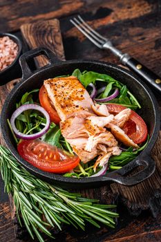 Grilled salmon fish fillet steak with fresh salad arugula, avocado and tomato in a pan. Dark wooden background. Top view.