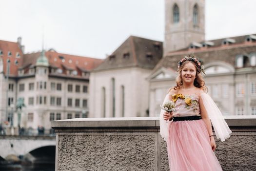 a little girl in a pink Princess dress with a bouquet in her hands walks through the old city of Zurich.Portrait of a girl in a pink dress on a city street in Switzerland.