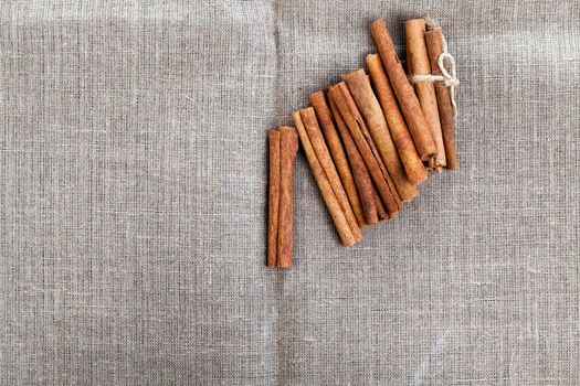 long sticks of cinnamon on a linen tablecloth crumbled from a tied bundle with a rope