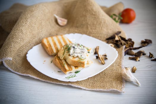 fried bread toast with cheese spread with boiled dried mushrooms, in a plate on a wooden table.